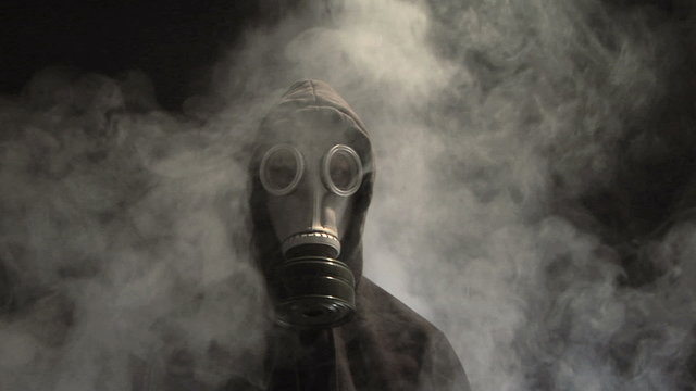 Smoke rising behind a man in a gas mask