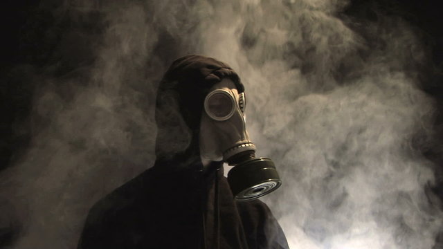 Smoke rising behind a man in a gas mask