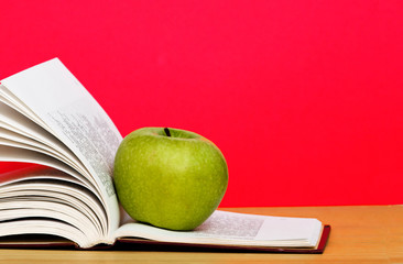 Green apple and open book on desk