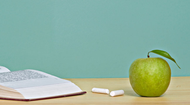 Green apple,  pieces of chalk, and open book on desk
