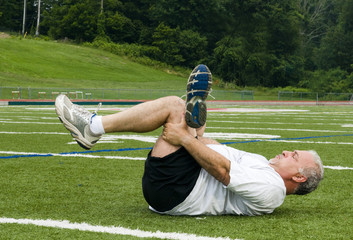 middle age man stretching after exercising on sports field