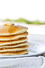 Stack of pancakes with syrup served outdoors.