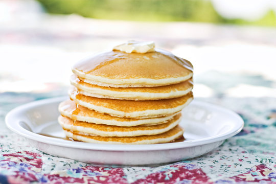 Stack of pancakes with syrup served outdoors.