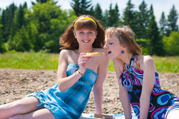 Two girls on a meadow eat a pizza