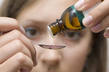 Dripping herbal essence of a vial over a spoon