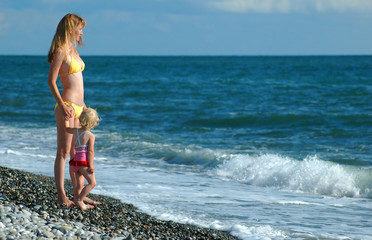 Woman and child in bikini stand on seaside