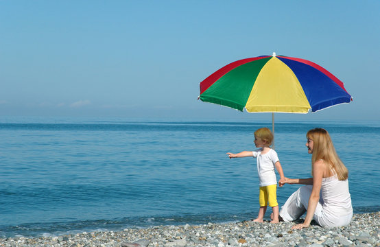 Woman With Child Under Umbrella On The Beach