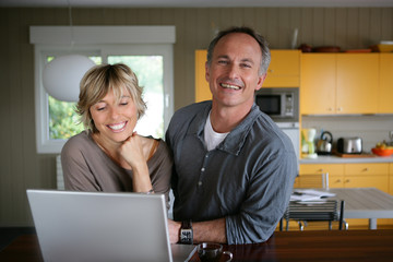 couple souriants devant un ordinateur portable dans une cuisine