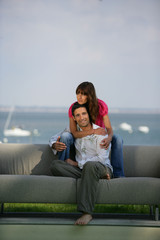 Homme et femme souriants assis sur un canapé dos à la mer