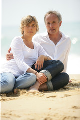 homme et femme assis sur le sable à la mer