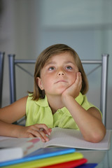 petite fille pensive assise à un bureau faisant ses devoirs