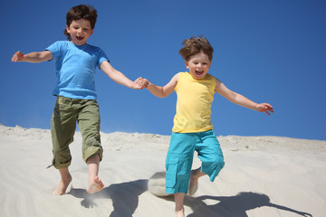 Two boys run on sand