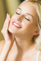 Smiling woman applying cream on face at home