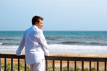 Young handsome man in white standing on a porch at the oceanfron