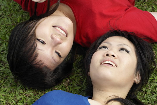 Two happy asian teen girls lying on grass in red and blue