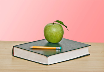 Green apple and pencil on top of book