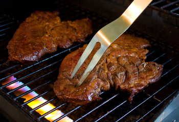 Steak on a grill with flames and grilling fork