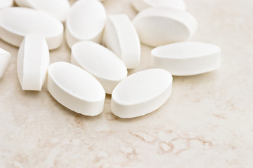 Fototapeta na wymiar White oval pills spilled onto the counter. Shallow DOF.