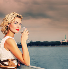 Beautiful blond girl drinks champagne near the river