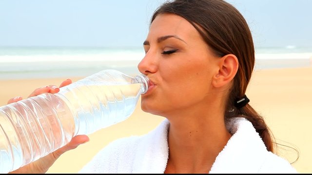 Jeune femme en peignoir buvant de l'eau sur la plage