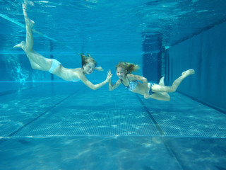zwei Mädchen tauchen fröhlich zueinander im Pool - obrazy, fototapety, plakaty