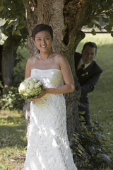 Bride in front and groom behind a tree