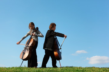 Two violoncellists play on grass against  sky © Pavel Losevsky