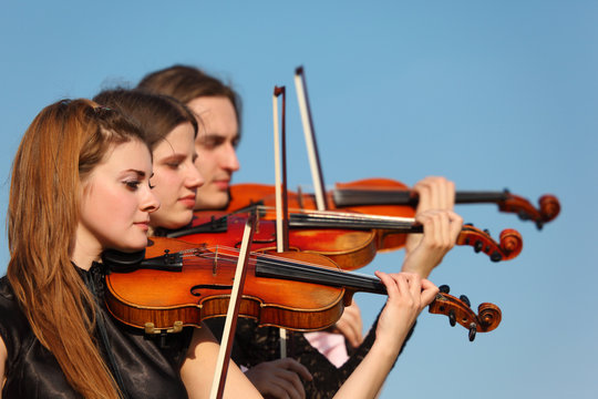 trio of violinists plays against sky