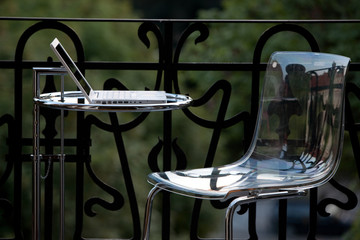 weißer Laptop auf rundem Glastisch und Plexiglasstuhl auf Balkon - 16341258