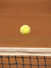 Tennis ball gliding over the net on clay court