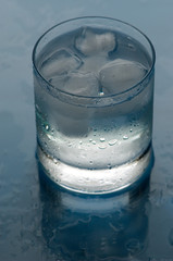 Water. A glass with water and an ice on a blue background