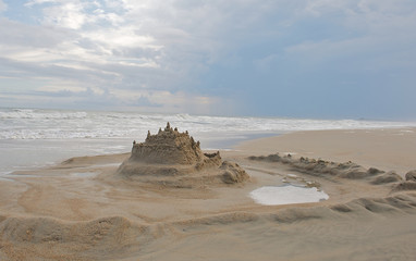Sand castle built on the beach with moat surrounding it.