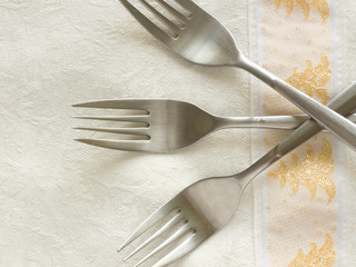 Three forks on the table cloth. Closeup.