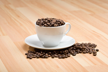 Cup with freshly roasted coffee beans on hardwood floor