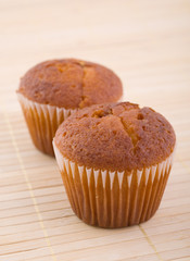 Two muffins on bamboo mat.