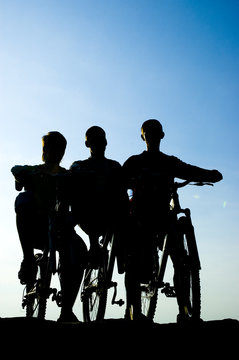 Silhouette of the bikers and bicycle on sky background.
