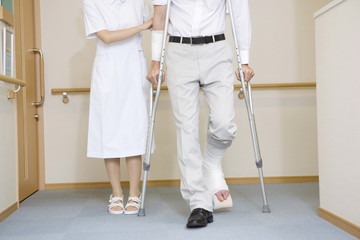 松葉杖をつく男性患者とフォローする看護師