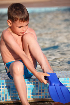 boy puts on flipperson border of pool