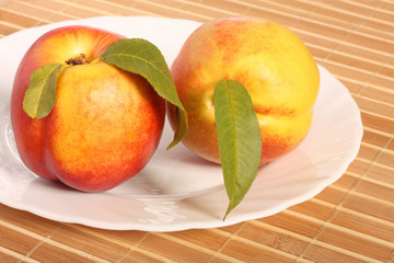 Two nectarine fruits with leaves on white plate