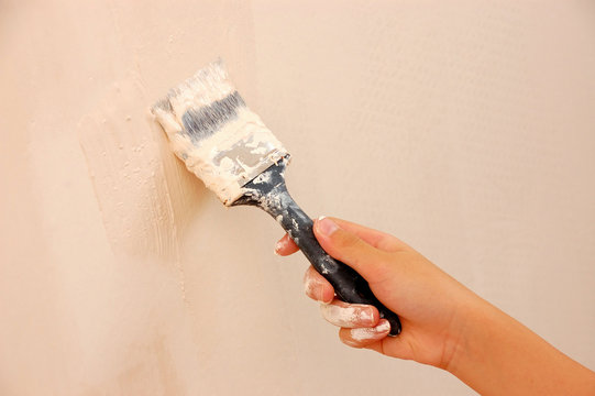 Child's Hand Holding Paintbrush and Painting Wall