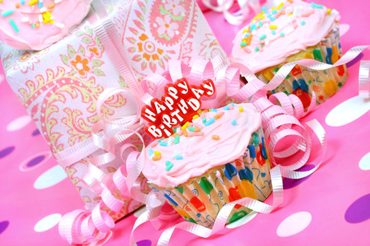 Pink birthday party cupcake with ribbons and gifts.