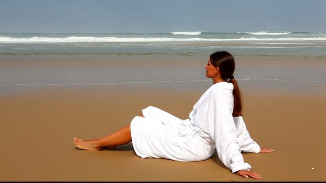 Jeune femme assise en peignoir sur la plage