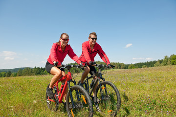 Plakat Sportive couple riding mountain bike in meadow
