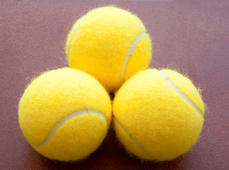 three tennis balls together in yellow on brown background.three