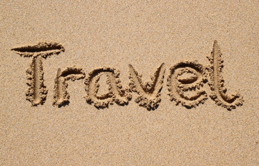 Travel written on a sandy beach.
