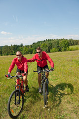 Fototapeta premium Sportive couple riding mountain bike in meadow