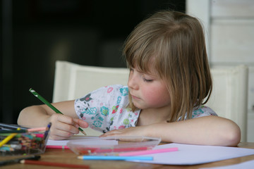 portrait d'une petite fille assise à table faisant du coloriage