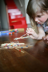 Portrait d'une petite fille couchée par terre jouant au mikado
