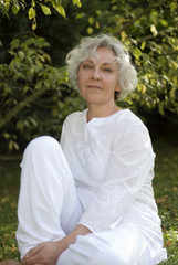 Seniorin sitzt im hellen Sommeroutfit in der Natur