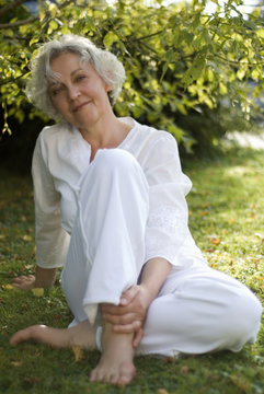 junggebliebene Seniorin sitzt entspannt lächelnd auf einer Wiese